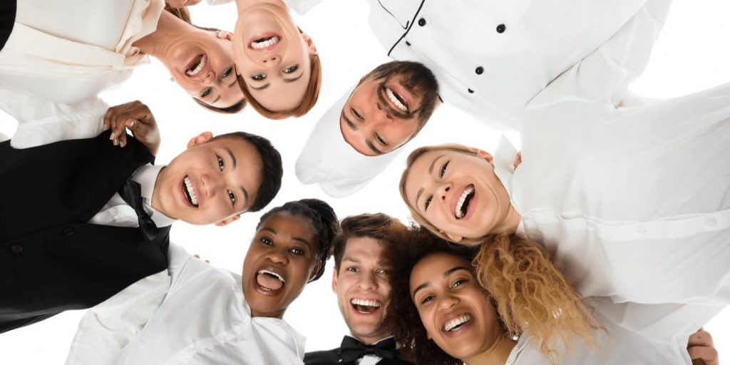 a diverse group of workers from hospitality jobs standing in a circle and smiling
