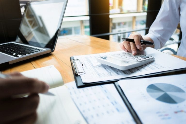 close-up image of financial documents and a calculator on a table while two accountants look over them