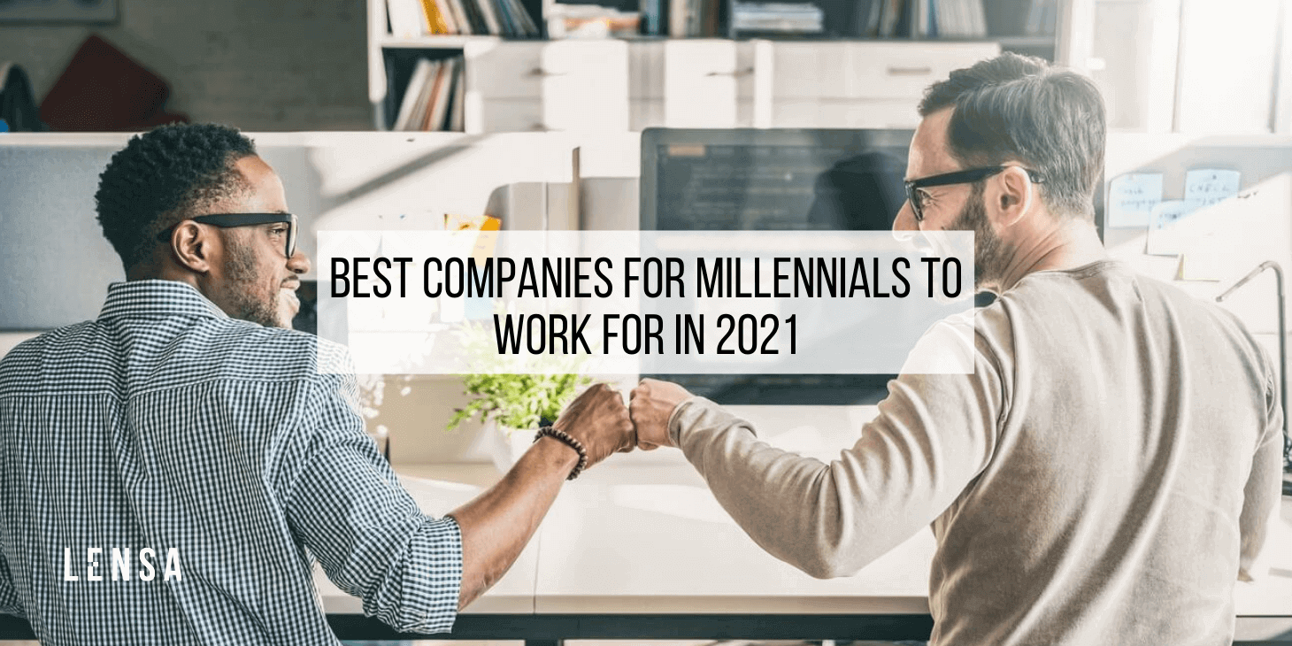 two millennials fist-bumping each other while sitting at their office desks at work