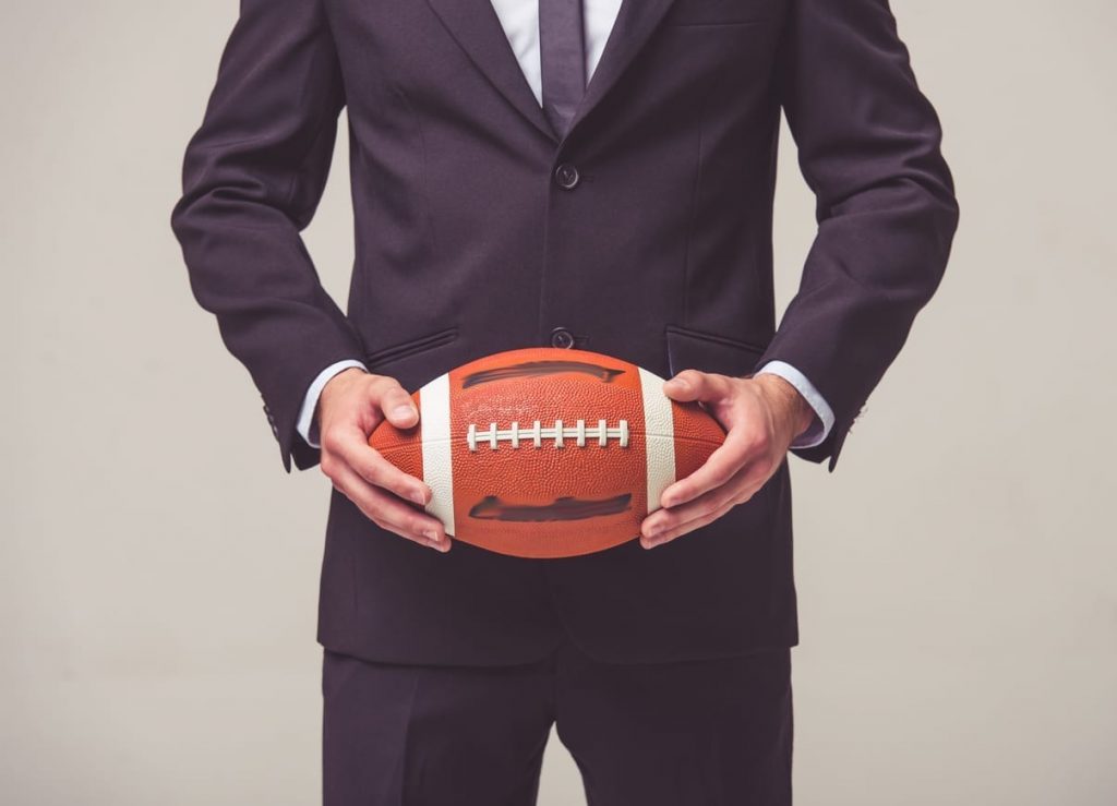 cropped image of a man in a business suit holding a football in detroit lions office