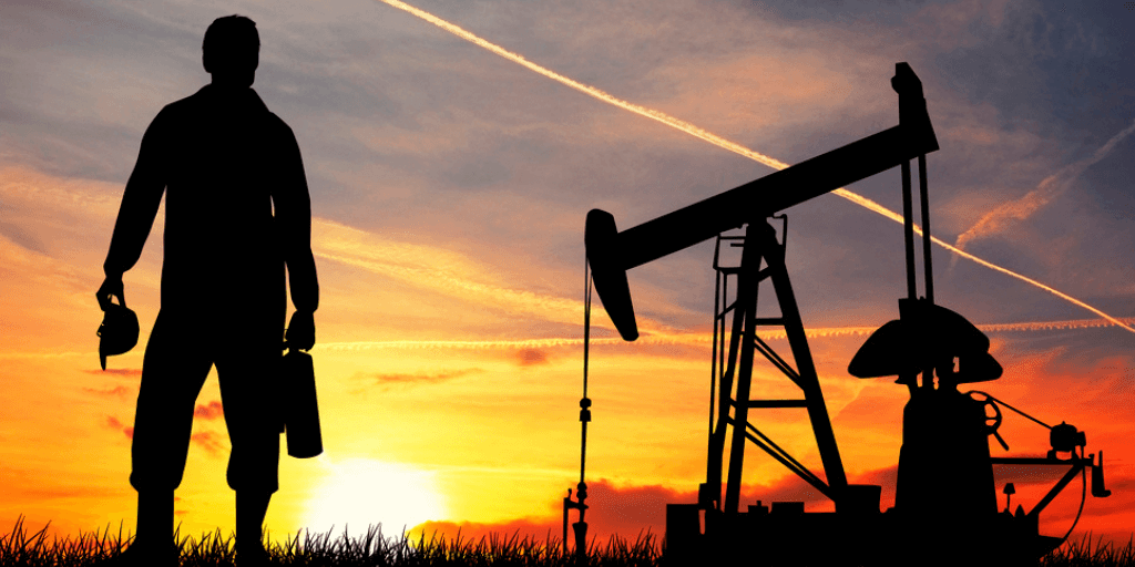 oil pump operator standing near an oil pump in the field at sunset
